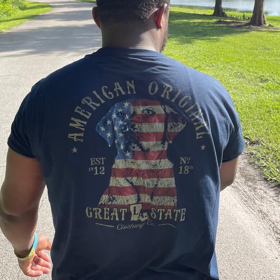 Lifestyle image of a man wearing the shirt walking down a road next to grass and trees.
