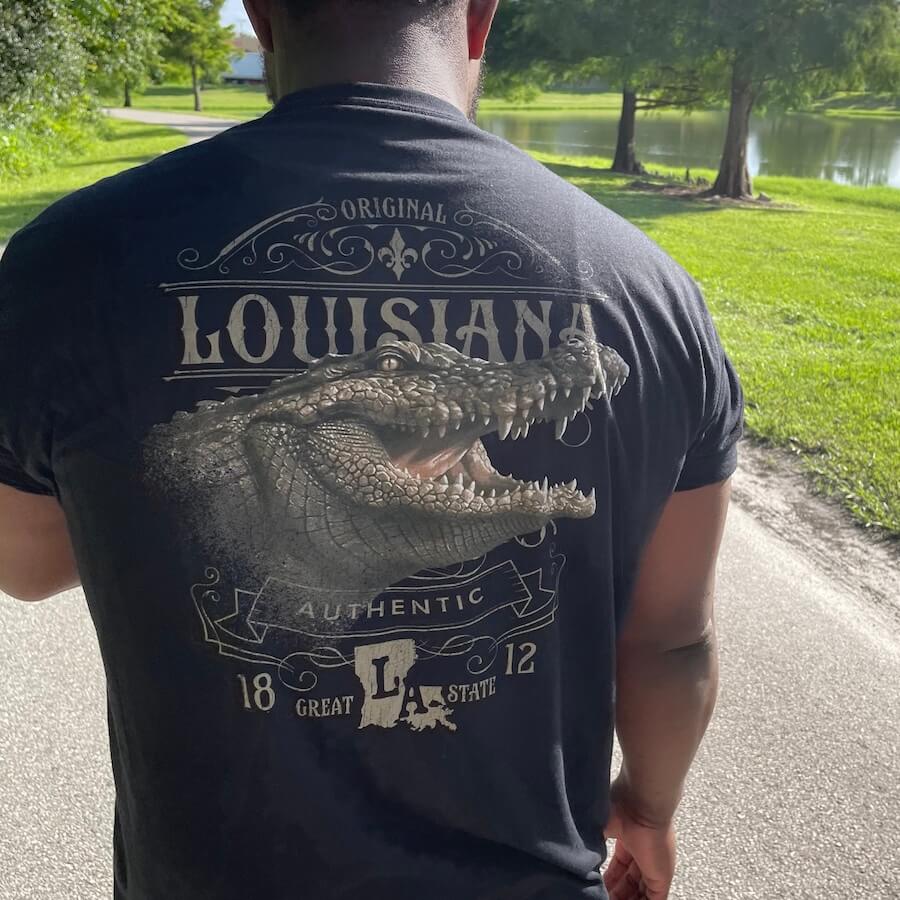 Lifestyle image of a man wearing the tee walking down a road next to a pond.